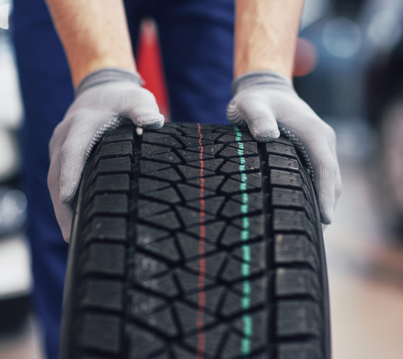 Closeup of mechanic hands pushing a black tire in the workshop.